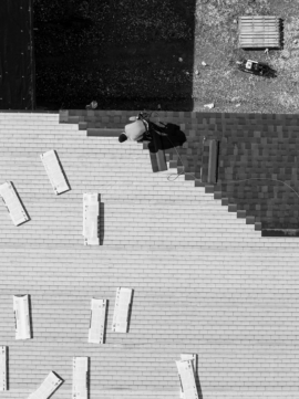 Aerial view of a roofer diligently working on a building, captured in stark black and white contrast.