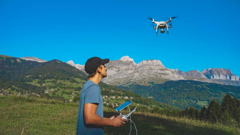 Drone operator with a remote control in a mountainous landscape, piloting a flying drone.