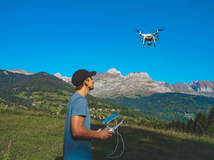 Drone operator with a remote control in a mountainous landscape, piloting a flying drone.